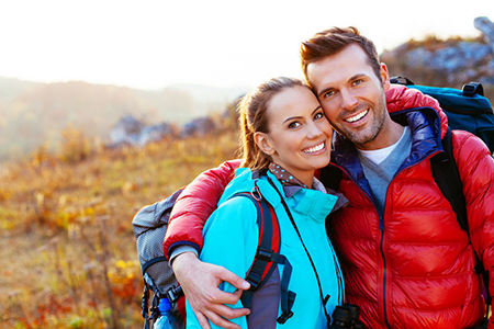Two adults, a man and a woman, posing for a photo outdoors with backpacks, smiling at the camera.